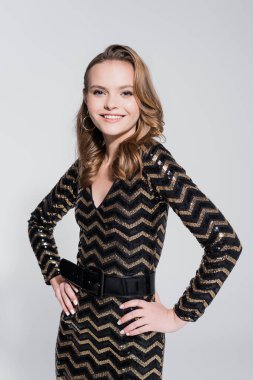 Mutlu bir kadın, elleri kalçasında gri renkte duruyor.