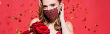 Koruyucu maskeli bir kadın. Elmas elmaslı. Güllerin yanında saç, kırmızı pankartta konfeti.