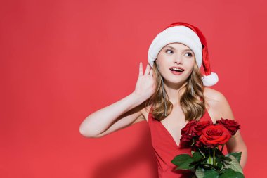 Noel Baba şapkalı mutlu genç bir kadın elinde güller ve kırmızıyı dinliyor. 