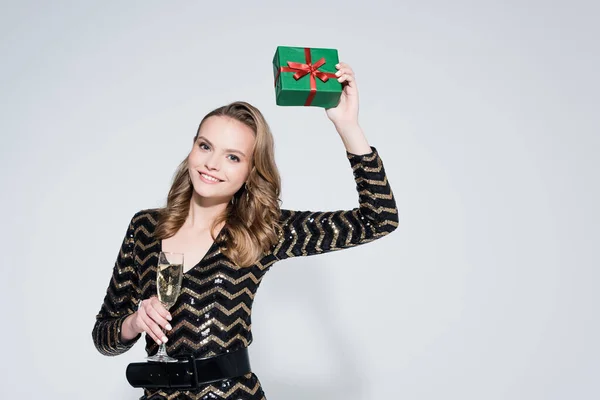 陽気な若い女性がシャンパンを持っているとグレーにプレゼントクリスマスを包んだ — ストック写真