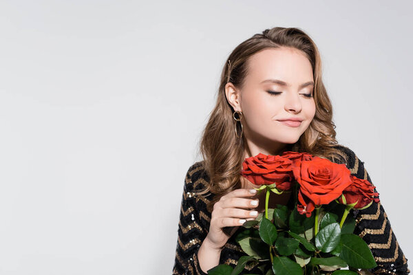 happy young woman smelling bouquet of red roses isolated on grey