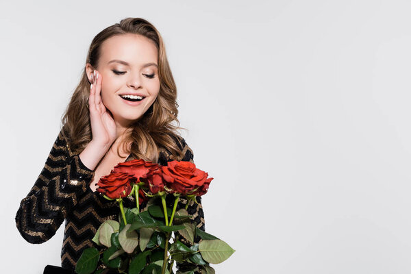 happy woman looking at bouquet of red roses on grey