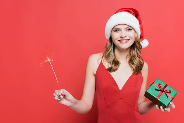 サンタ ハットの陽気な女性クリスマスプレゼント箱とキラキラOn赤 — ストック写真