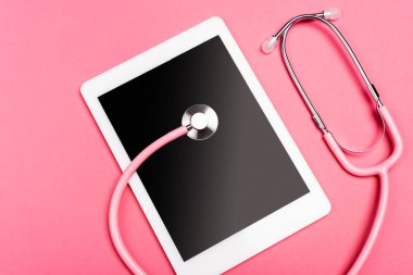 Dijital tablette steteskopun üst görünümü ve pembe arkaplanda boş ekran