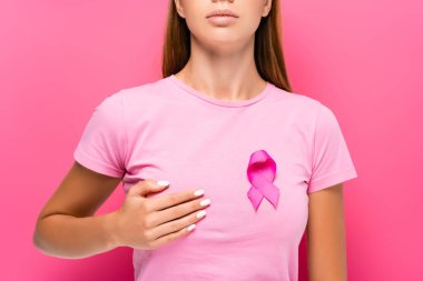Göğüs kanseri olan genç bir kadının pembe arka planda göğüslerine dokunan kurdeleli görüntüsü. 