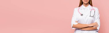 Beyaz önlüklü, steteskoplu ve kollarını çapraz bağlayan pembe pankarttaki doktor görüntüsü. 