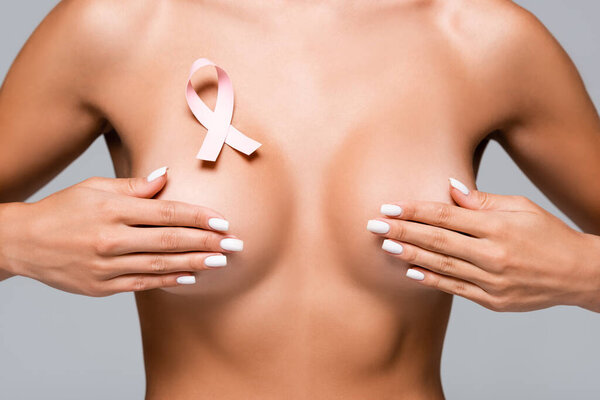 Cropped view of nude woman with breast cancer ribbon touching bust isolated on grey 