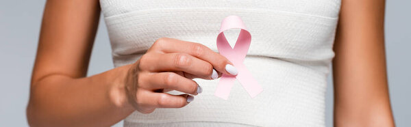 Обрезанный вид женщины с эластичной повязкой на бюсте, держащей ленту осведомлённости о раке молочной железы изолированной на сером, баннер