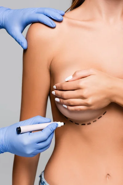 灰色に隔離された若い女性の胸の近くにマーカーを保持する形成外科医の作物ビュー — ストック写真