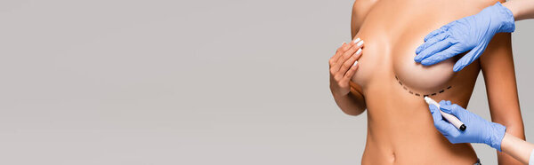 Cropped view of plastic surgeon marking line on breast of nude woman isolated on grey, banner 