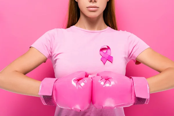 Cropped view of young woman in pink boxing gloves and ribbon of breast cancer awareness on pink background