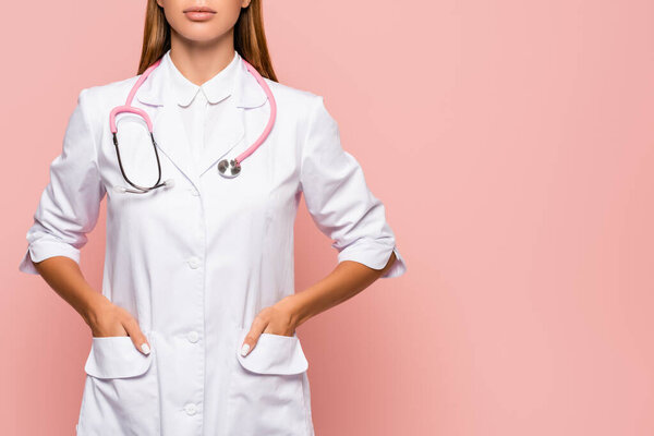 Cropped view of doctor with stethoscope and hands in pockets of white coat isolated on pink