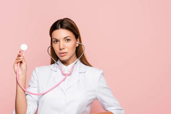 Morena Médico Olhando Para Câmera Enquanto Segurando Estetoscópio Isolado Rosa — Fotografia de Stock