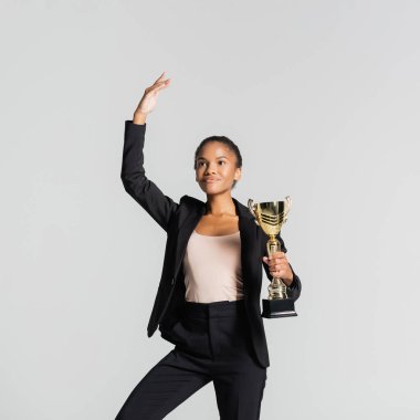 smiling african american businesswoman performing ballet with golden cup isolated on grey clipart