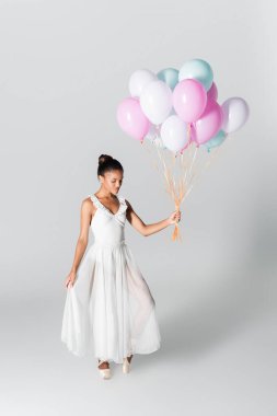 Beyaz arka planda balonlarla dans eden zarif Afrikalı Amerikalı balerin.