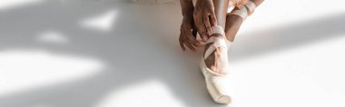 cropped view of graceful african american ballerina in pointe shoes sitting on floor on white background, banner clipart