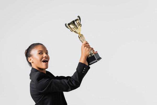 happy african american businesswoman with golden cup isolated on grey