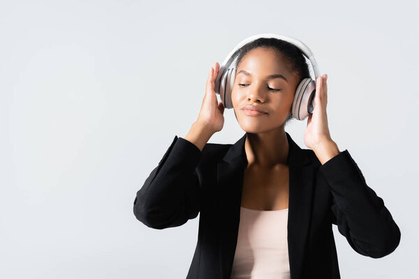african american businesswoman listening music in headphones isolated on grey