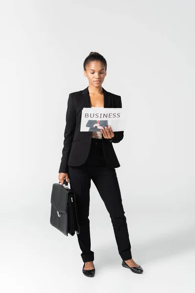 グレーで隔絶されたビジネス新聞を読むスーツケースを持つアフリカ系アメリカ人のビジネスウーマン — ストック写真