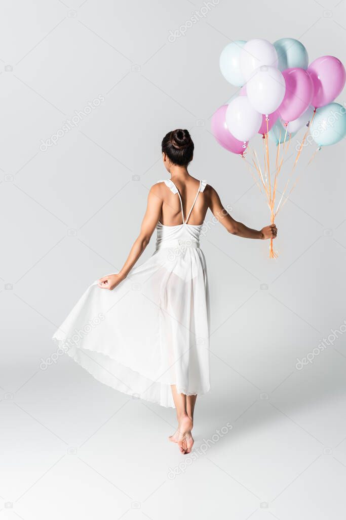 back view of barefoot graceful african american ballerina in dress with balloons on white background