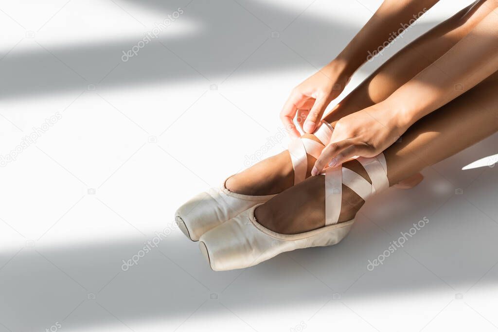 cropped view of graceful african american ballerina in pointe shoes sitting on floor on white background