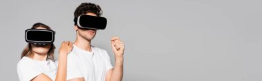 Gri pankartta izole edilmiş beyaz tişörtlü ve vr kulaklıklı sıradan genç çift