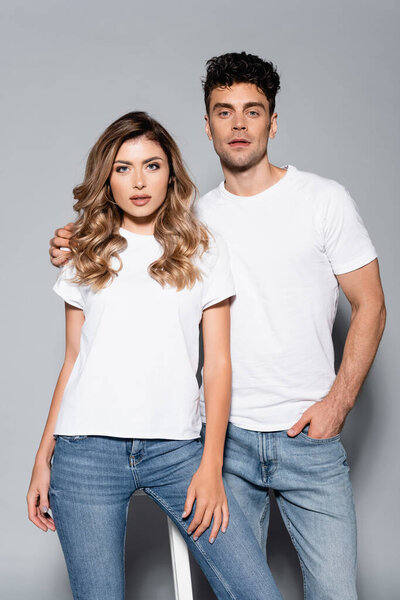 young couple in white t-shirts and jeans posing isolated on grey