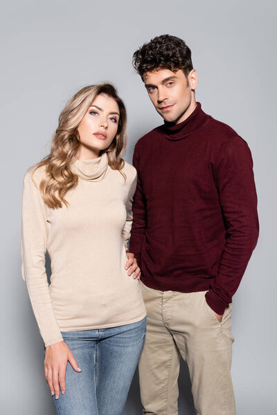 casual young couple in turtleneck jumpers posing isolated on grey