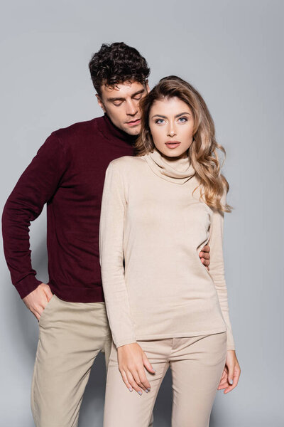 casual young couple in turtleneck jumpers posing isolated on grey