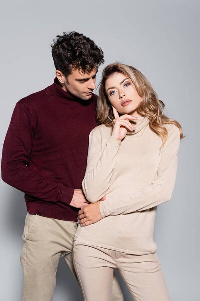 casual young couple in turtleneck jumpers posing isolated on grey