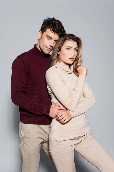 casual young couple in turtleneck jumpers embracing isolated on grey