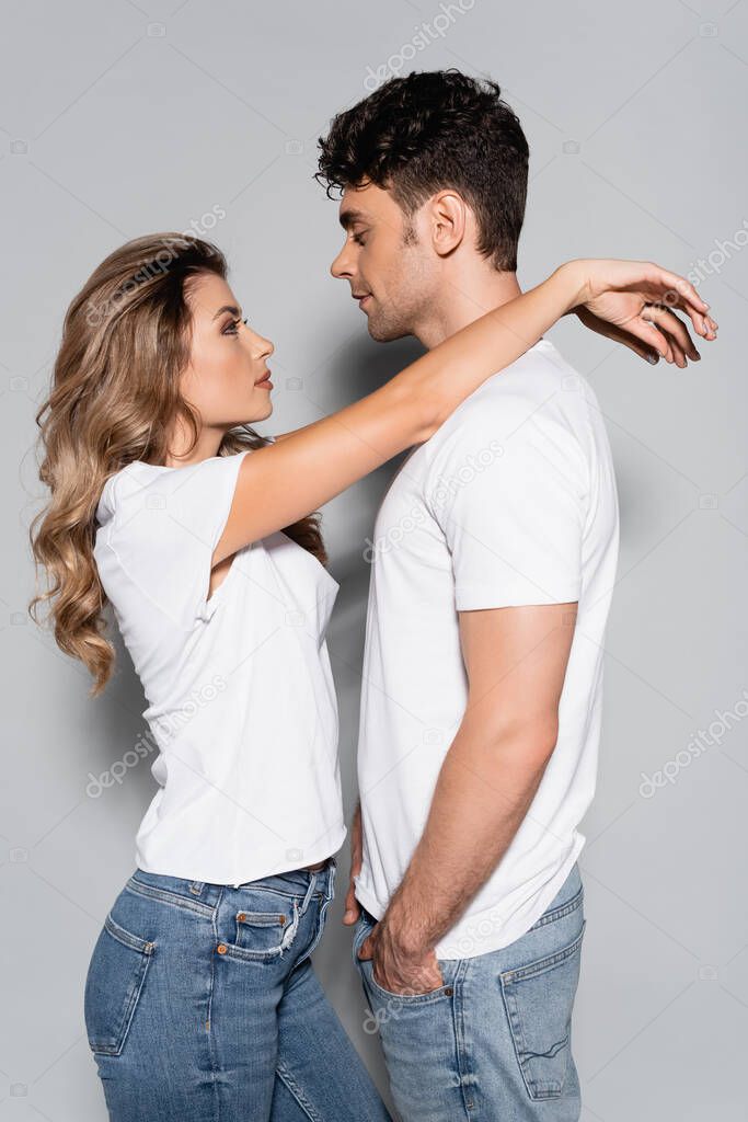 side view of young couple in white t-shirts hugging isolated on grey