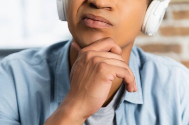 Kablosuz kulaklık takmış düşünceli Afro-Amerikan bir adam podcast dinliyor. 