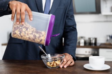 partial view of african american businessman holding container with corn flakes near bowl clipart