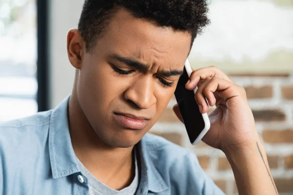 upset african american man talking on smartphone