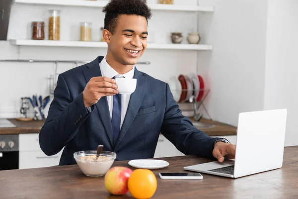Glad Afrikansk Frilansare Kostym Använder Laptop Medan Äter Frukost — Stockfoto