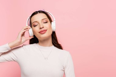 happy young pretty woman in headphones touching belly isolated on pink clipart