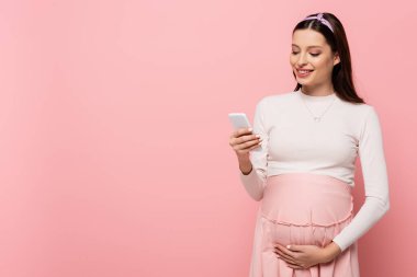 Pembe üzerine izole edilmiş akıllı telefon kullanan mutlu, güzel, hamile bir kadın.
