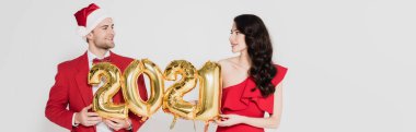 Gülen kadın, elinde 2021 numaralı balonlarla Noel Baba şapkalı adamın yanında gri pankartta izole bir şekilde duruyor. 