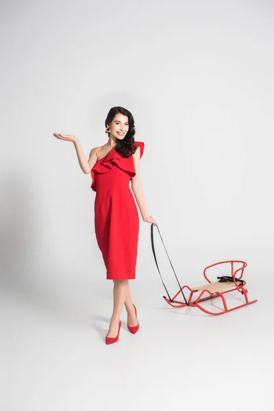 Cheerful Woman Red Dress Heels Holding Sleigh Grey Background — Stock Photo, Image
