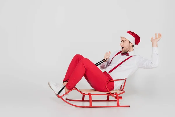 Spännande Man Santa Hatt Och Fluga Sitter Släde Grå Bakgrund — Stockfoto