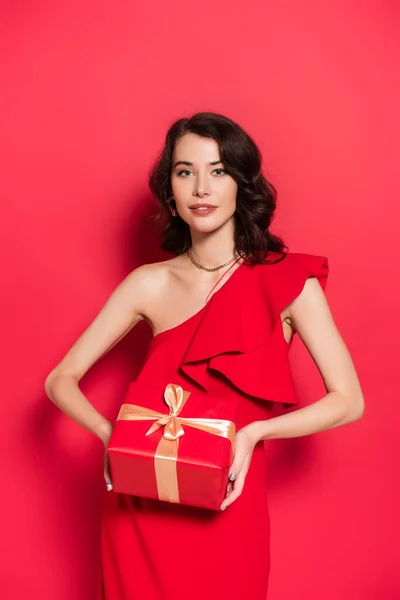 Brunette Vrouw Glimlachen Terwijl Het Vasthouden Van Cadeau Rode Achtergrond — Stockfoto