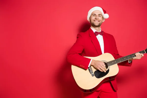 Glimlachende Man Santa Hoed Spelen Akoestische Gitaar Rode Achtergrond — Stockfoto
