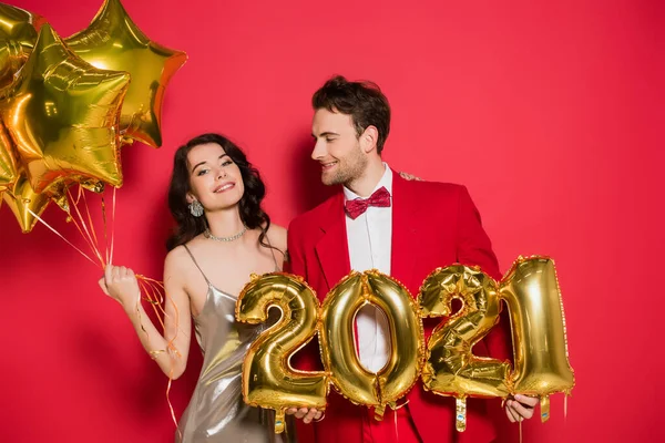 笑着的女人看着靠近男友的相机 带着2021年红色背景数字形状的气球 — 图库照片