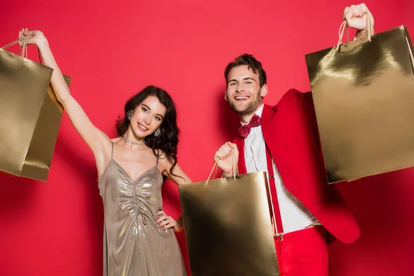 Cheerful Couple Looking Camera While Holding Shopping Bags Red Background — Stock Photo, Image