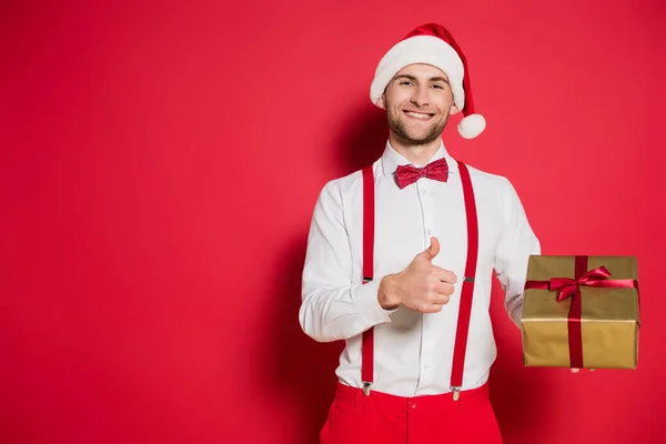 Sonriente Hombre Santa Hat Mostrando Como Gesto Mientras Sostiene Regalo — Foto de Stock