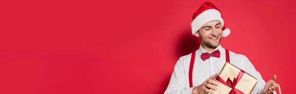 Usmívající Muž Santa Klobouk Drží Dárek Červeném Pozadí Prapor — Stock fotografie
