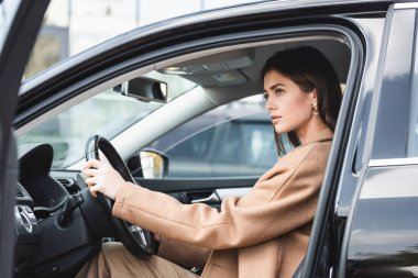 Sonbahar kıyafetli şık bir kadın bulanık ön planda arabada otururken gözlerini kaçırıyor.