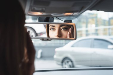 woman in car touching face while looking in rearview mirror on blurred foreground clipart