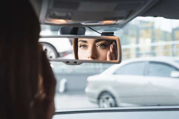 前景のぼやけた鏡を見ながら車の中で顔を触る女性 — ストック写真